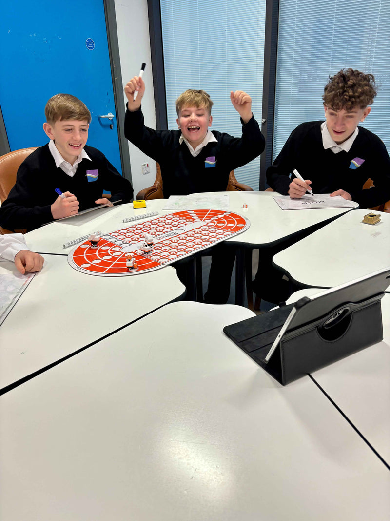 Three children in school uniforms sitting around a table with a large red and orange board game.