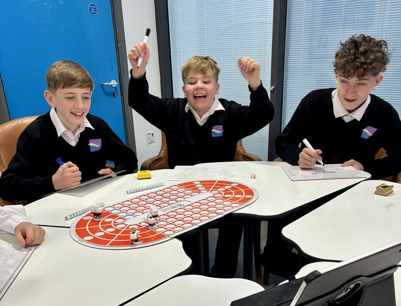 Three children in school uniforms sitting around a table with a board game, smiling and laughing.